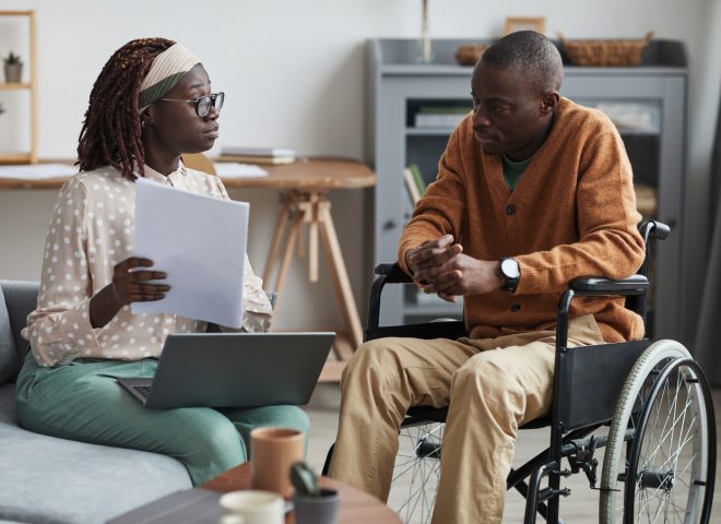 Portrait of African-American couple with handicapped man using wheelchair working from home together in modern interior