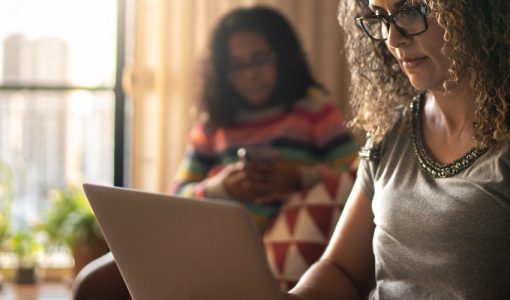 woman sitting on laptop with daughter in background