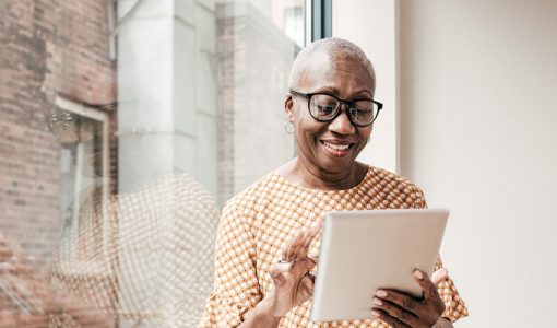 african american older woman with glasses on, reading news on tablet by window